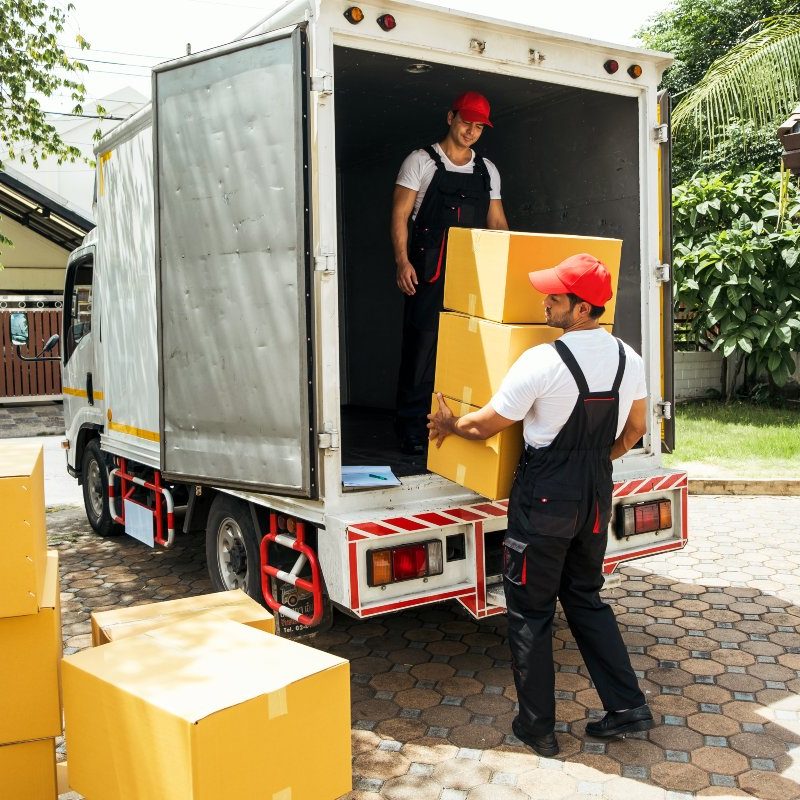 Asian and Caucasian workers in uniform unloading cardboard boxes from the truck. Delivery men unloading boxes and check the checklist with their coworkers. Professional delivery and moving service.